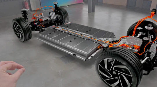 A hand makes a pinching gesture to interact with a 3D projection of the drivetrain of a car