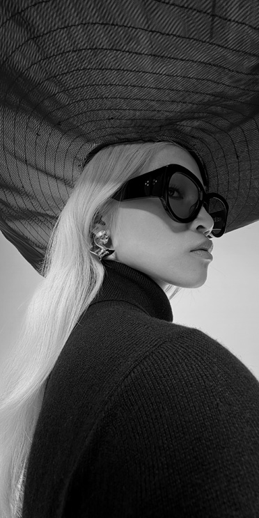 Close-up black and white photo of person in sunglasses and large hat